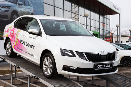 A car with an advertisement on its body stands on a podium near the glass facade of a car dealership on a spring street.のeditorial素材