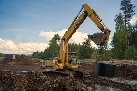 The excavator is carrying a concrete ring to install a sewer well in a pipeline at a construction site.のeditorial素材