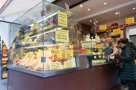 An adult woman is shopping at a grocery store, with a glass display case with cheese in the foreground.のeditorial素材
