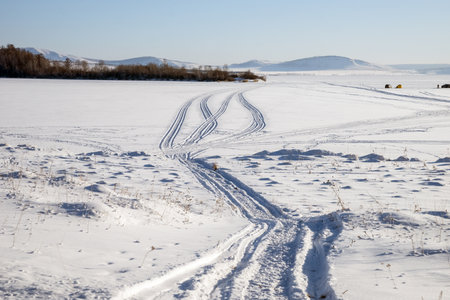 Trace from snowmobile on a snowy lake with fishermen in the backgroundの写真素材