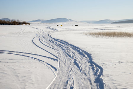 Trace from cars on a snowy lake with fishermen in the backgroundの写真素材
