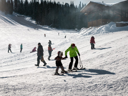 Mom teaches a child to ski among other vacationers at a ski resort on a sunny winter day.のeditorial素材