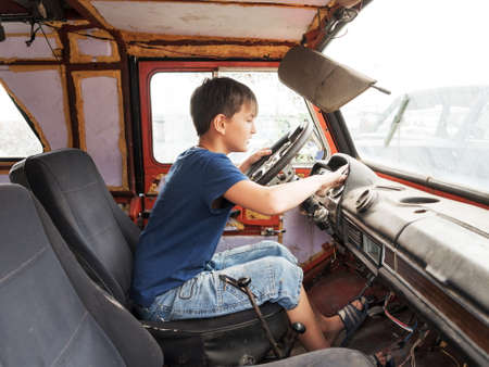 An 11-year-old boy plays as a driver behind the wheel of an old abandoned car.の写真素材