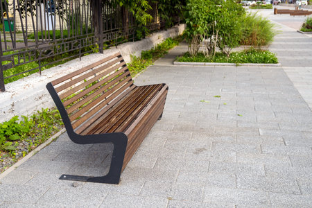 An interestingly designed street bench stands on the asphalt next to a metal fence.
