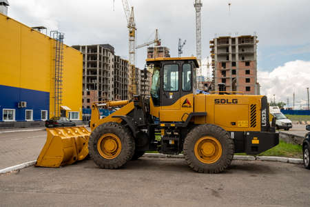 Krasnoyarsk, Krasnoyarsk Region, RF - July 20, 2021: A wheel loader stands in front of a construction site with high-rise buildings and tower cranes on a cloudy summer day.のeditorial素材