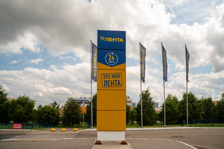 Krasnoyarsk, Krasnoyarsk Region, RF - July 20, 2021: Stella and flags with the logo and the name of the Lenta supermarket in Russian sway in the wind against the backdrop of trees on a summer day.のeditorial素材