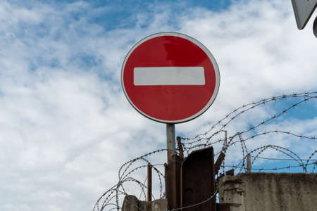 No entry road sign is located on a concrete fence with barbed wire against the background of a beautiful sky.の写真素材
