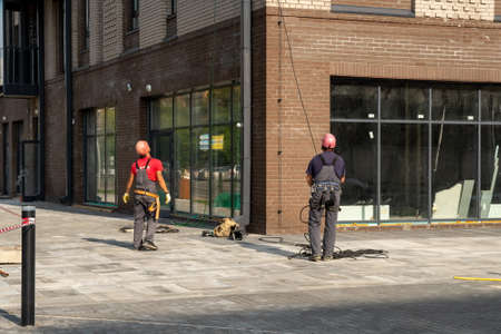 Krasnoyarsk, Krasnoyarsk Region, RF - July 19, 2021: Two working installers in helmets with safety belts remove the cable after working at heights on a residential building under construction.のeditorial素材