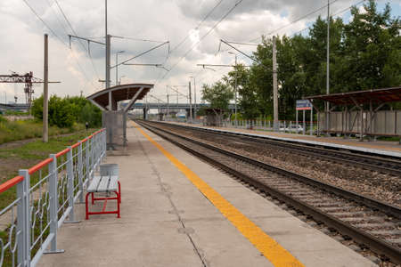 Krasnoyarsk, Krasnoyarsk Region, RF - July 20, 2021: Deserted platform of the Severnoye Highway station for an electric train with rails extending into the distance on a cloudy summer day.のeditorial素材