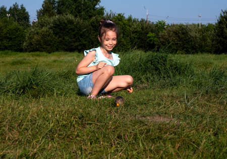 Krasnoyarsk, Krasnoyarsk Region, RF - July 24, 2021: The girl smiles, looking at the gopher, gnawing a carrot, in the meadow among the green grass in summer.のeditorial素材