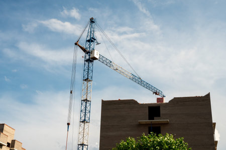 A tower crane rises above a brick apartment building under construction against the sky on a summer day.の写真素材