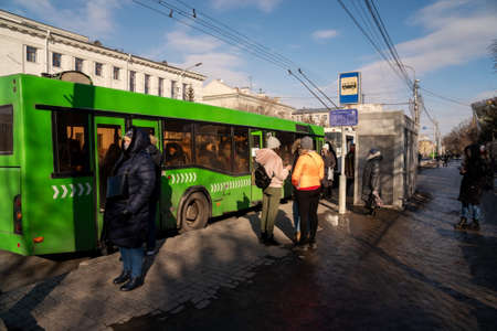 Krasnoyarsk, Krasnoyarsk Region, RF - March 14, 2021: Bus stop Cinema Luch with a white trolleybus and a green bus slowing down and people waiting on Prospekt Mira on a spring day.のeditorial素材