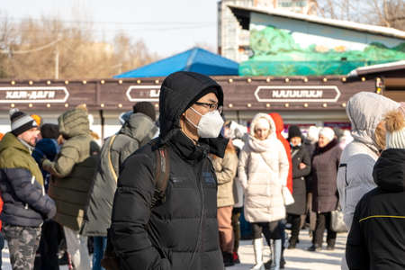 Krasnoyarsk, Krasnoyarsk Region, RF - March 14, 2021: A young man of Asian ethnicity stands in a medical protective mask among a crowd of people without masks on a city street in spring.のeditorial素材