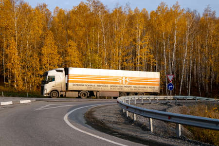 Achinsk, Krasnoyarsk Region, RF - October 6, 2019: A cargo van drives on a highway against the backdrop of a yellow birch forest in autumn.のeditorial素材