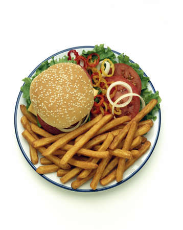 Cheese hamburger on a sesame seed bun and fries with tomatoes, onions, lettuce, and hot pepper side salad overhead on white with copy spaceの写真素材