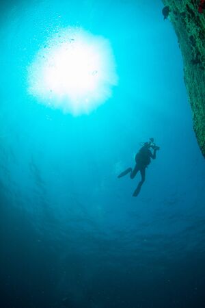 Scuba Divers, silhouettes against sunburst, in the ocean beside coral reefの写真素材