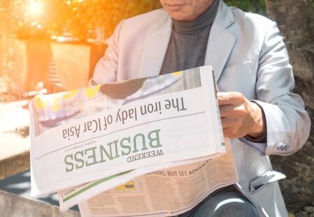 business, press, news  and concept - close up of businessman reading newspaper under treeの写真素材