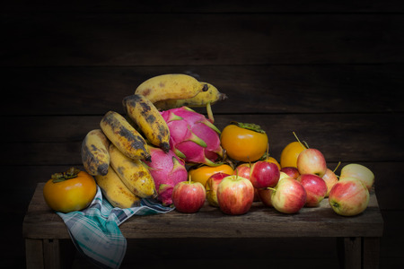 Still life of skull, apples, banana, dragon fruit, Persimmon, cloth and candle on wooden tableの写真素材