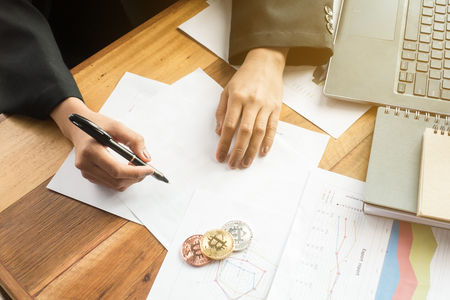 close up of business woman hand write on paper with laptop computer, Bitcoin, business graph information diagram on wooden desk as concept in morning lightの写真素材