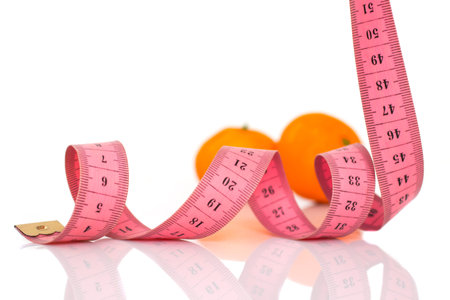 orange fruits and measuring tape on a white background to symbolize a healthy dietの写真素材