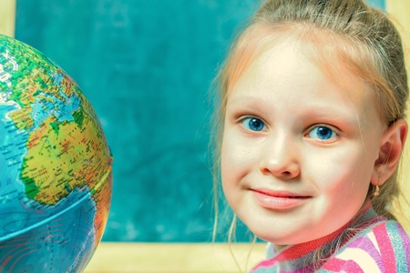 girl - a child of seven years on the geography lesson near  globe  the world against the background  the school boardの写真素材