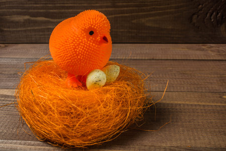 Orange toy chicken near a decorative nest with an egg on a wooden textureの写真素材