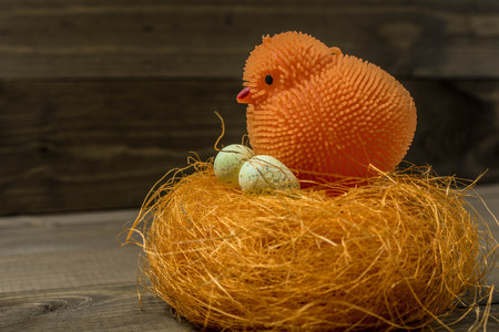 Orange toy chicken near a decorative nest with an egg on a wooden textureの写真素材