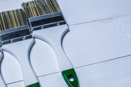 A set of paint brushes and a jar with white paint on a textured wood table