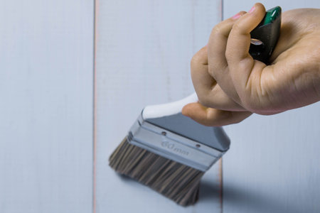 Baby hand holds a paint brush on a white wooden background