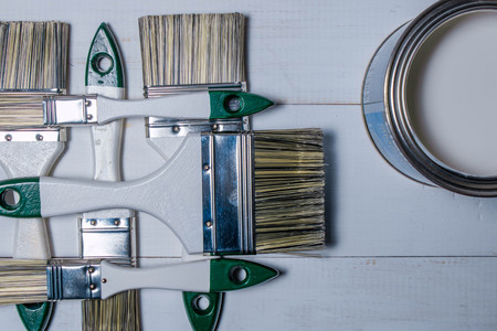 A set of paint brushes and a jar with white paint on a textured wood tableの写真素材