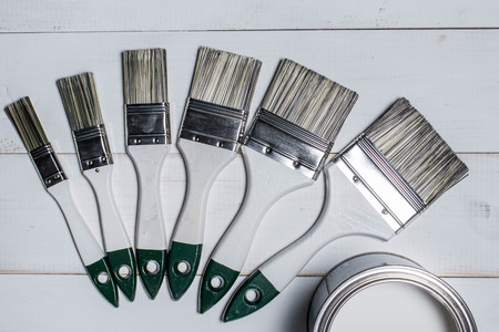 A set of paint brushes and a jar with white paint on a textured wood tableの写真素材