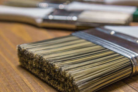 A set of white paint brushes, a metal can with white paint on a wooden table