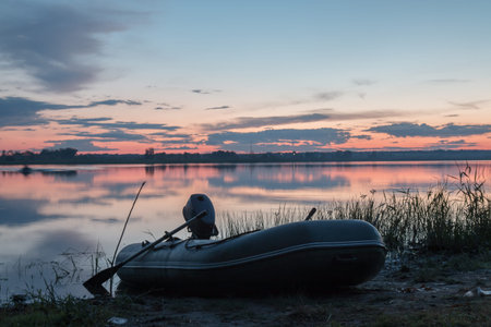 The inflatable boat with the motor moored near the shore of the pond at sunset