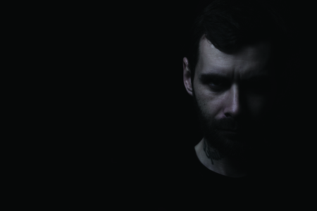 Portrait of young brutal man with a beard, with a textured face on a black background. Left side of the frame free textの写真素材