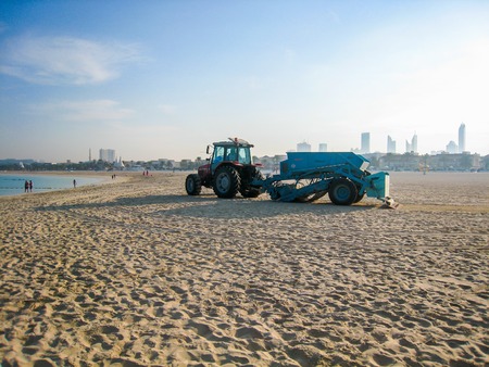 tractor picking up trash on the sandy beach in Dubai, UAE at dawnの写真素材