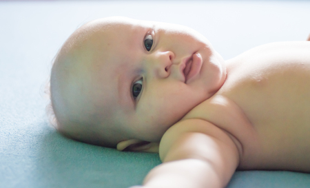 portrait of a beautiful newborn baby who smiles on a blue sheet in diapersの写真素材