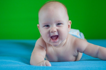portrait of a beautiful newborn baby who smiles on a blue sheet in diapersの写真素材