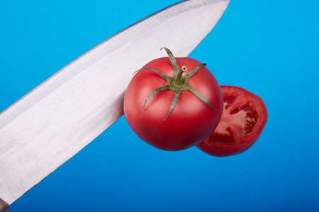 A ripe tomato cut with a sharp knife on a blue backgroundの写真素材