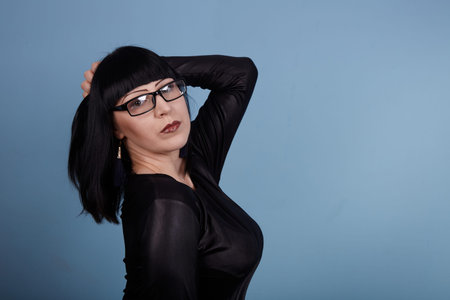 portrait of a beautiful girl with glasses posing for a photographer in the studio on a blue...
