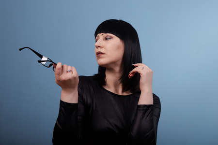 portrait of a beautiful girl with glasses posing for a photographer in the studio on a blue backgroundの写真素材