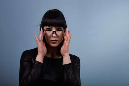 portrait of a beautiful girl with glasses posing for a photographer in the studio on a blue backgroundの写真素材