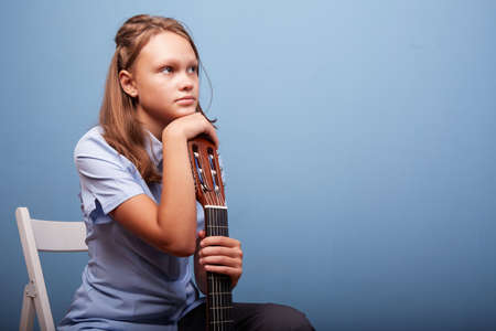 an 11-year-old girl is practicing a melody on a guitar on a blue backgroundの写真素材