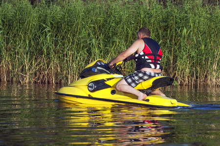 Man rolling around on the lake on a yellow jet ski along the reedsの写真素材