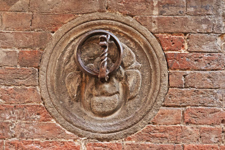 Ancient door knocker on a brick wall in Siena, a medieval town in Tuscany, Central Italyの写真素材