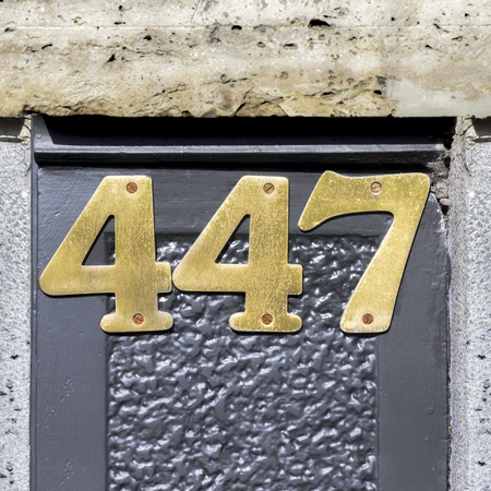 brass house number four hundred forty-seven, screwed against a gray wallの写真素材