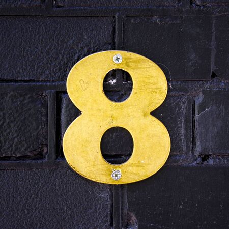 brass house number eight attached to a black painted wall の写真素材