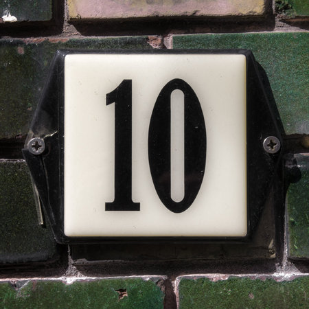 enameled plate with the house number ten, attached to a wall of green bricks.の写真素材