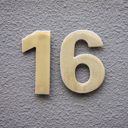Brass house number sixteen on a plastered wall.の写真素材