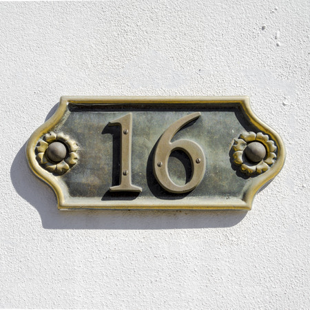 cast bronze house number sixteen on a white stucco wallの写真素材