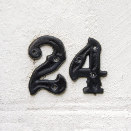 cast metal house number twent four. Separate black numerals on a white stucco wallの写真素材